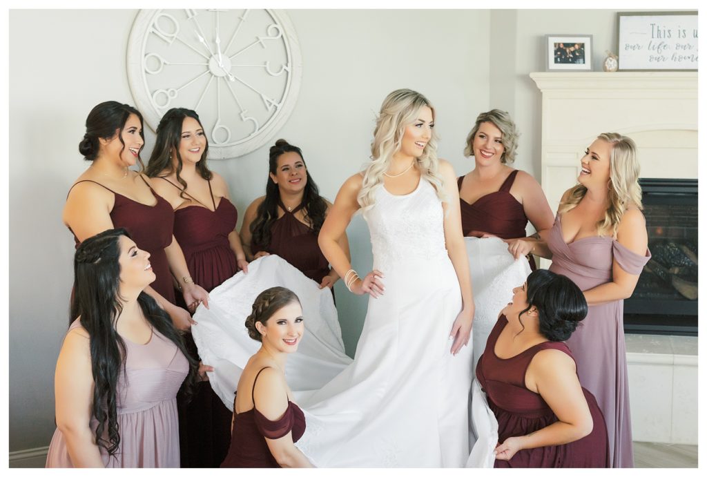 bridesmaids wearing burgundy bridesmaids dresses help a bride get ready before her wedding at JEH Ranch