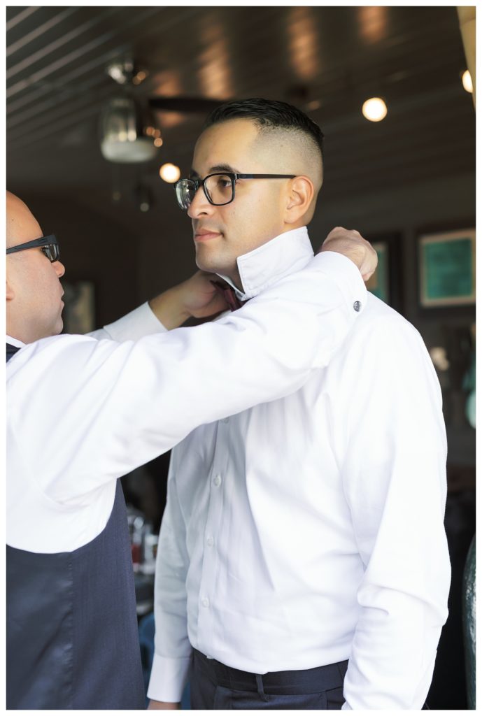 a groomsman helps a groom get ready before a wedding at JEH Ranch