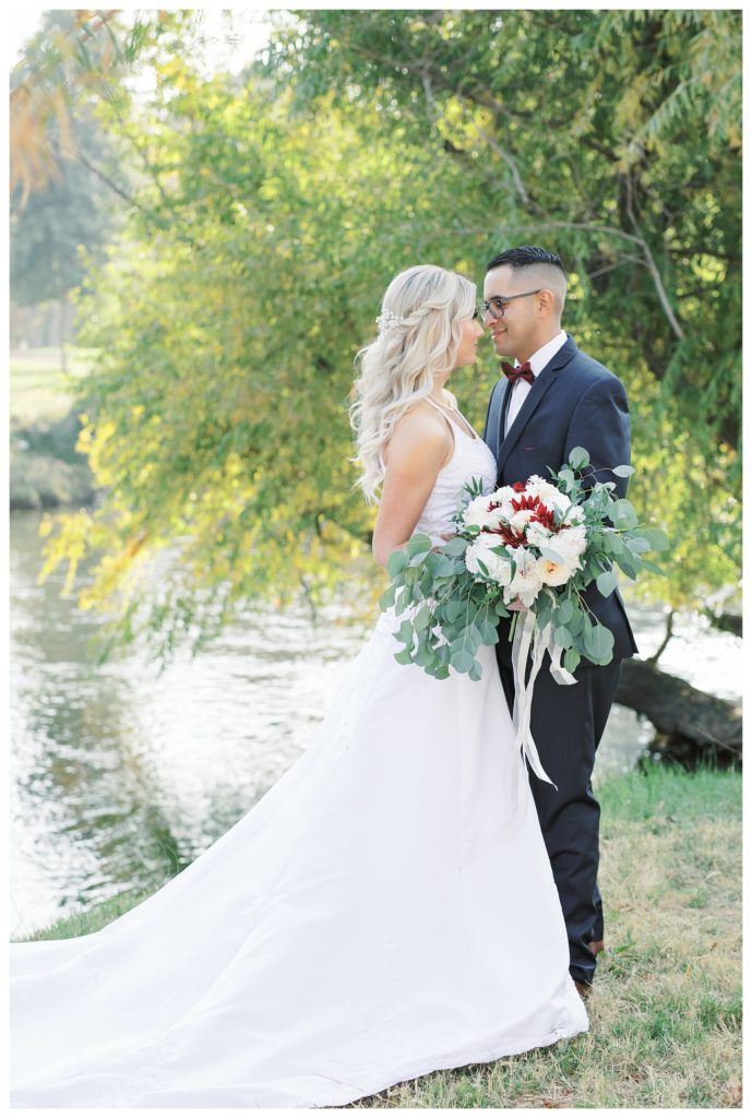 a bride and groom pose next to a river at their wedding at JEH Ranch