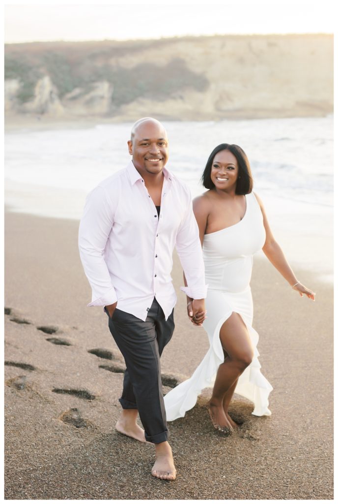 a couple walks along the beach during their engagement photos at Montaña de Oro State Park