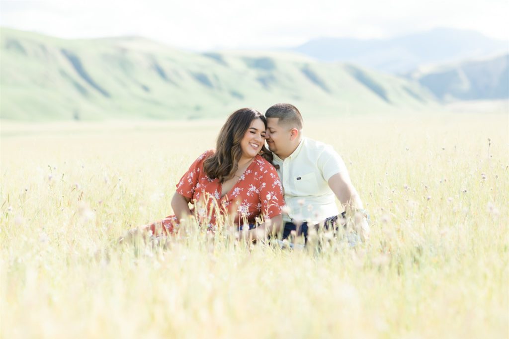 a couple sits in a field during engagement photos at Wind Wolves Preserve