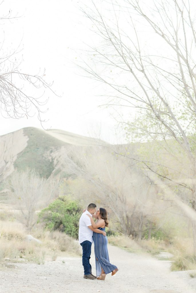 a man kisses a woman in front of the mountains during engagement photos at Wind Wolves Preserve