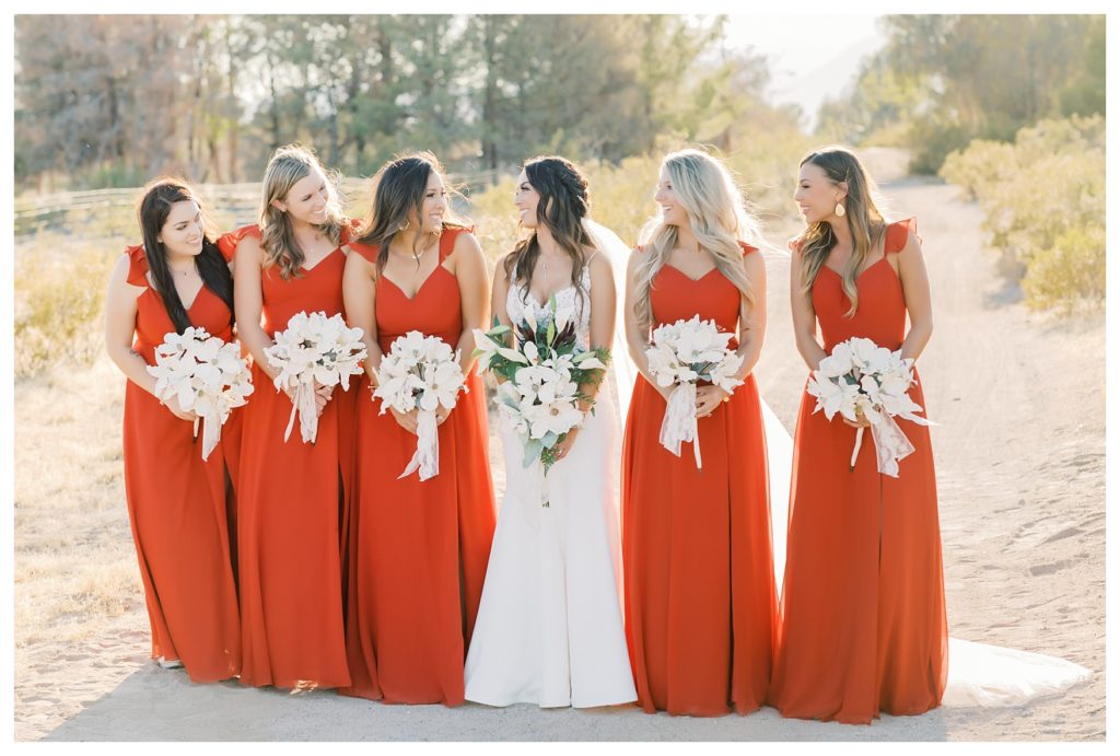 a bride poses with her bridesmaids in burnt orange dresses during her rescheduled COVID wedding